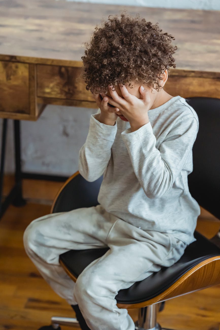 A child sits looking troubled and in pain - pain is listed as one of the key symptoms of paediatric fibromyalgia.